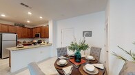 This single-floor residence offers a thoughtfully designed layout with interconnected living spaces that promote a natural flow throughout the home. The kitchen is equipped with rich medium-toned wood cabinetry, stainless steel appliances including a refrigerator, range, and microwave, and granite-style countertops that extend to a peninsula with a double sink — an ideal setup for cooking and casual interaction. Light tile flooring anchors the kitchen, which also includes a pantry closet for added storage.

Adjacent to the kitchen, the dining area comfortably accommodates a round table and tufted upholstered chairs, creating an inviting space for meals. The living room features carpet flooring, a ceiling fan, and a large window that draws in natural light, contributing to a bright and airy atmosphere.

Both bedrooms are carpeted and well-lit by generously sized windows with vertical blinds, offering ample natural light. Ceiling fans in each room add comfort and functionality. The two bathrooms mirror the home's consistent design, featuring granite-topped vanities with warm wood cabinetry and tile flooring. One bathroom includes a tub-shower combination. A hallway connects the private areas of the home, maintaining a clear separation between living and sleeping spaces.