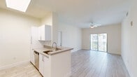 Located at 26710 SW 140th Ave, Unit 304 in Homestead, FL, this two-bedroom, two-bathroom residence offers a well-organized layout across a single primary floor. The open-concept living area is bright and airy, anchored by light wood-style tile flooring that extends throughout the unit. The kitchen is equipped with white cabinetry, stainless steel appliances including a full-size refrigerator, a built-in dishwasher, and a peninsula countertop with a neutral gray surface — ideal for casual dining or meal prep. A pendant light fixture and a skylight above add warmth and natural illumination to the space. The living room flows seamlessly toward sliding glass doors that open onto a private balcony, where palm-lined community views and Florida's open skies can be enjoyed. A ceiling fan overhead keeps the living area comfortable year-round. The primary bedroom features a mirrored sliding closet, elevated ceilings, and its own access to the hallway. Both bathrooms are cleanly finished, with one featuring a full tub-shower combination with white tile surround. Additional highlights include a dedicated laundry area, a utility room, and two closets for ample storage throughout the unit.
