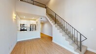 This two-story residence in Los Angeles' East Hollywood neighborhood offers a thoughtfully designed layout with clean, modern finishes throughout. The main level opens into a bright, open-concept living area anchored by warm hardwood-style flooring and soaring double-height ceilings that create an expansive, airy atmosphere. A sleek kitchen sits adjacent to the living space, featuring white shaker cabinetry, a subway tile backsplash, stainless steel appliances including a gas range and refrigerator, and a generous peninsula with a crisp quartz countertop and an undermount sink — ideal for both cooking and casual dining. A carpeted staircase with a contemporary metal railing leads to the upper level, where the bedrooms are situated. Each bedroom is finished with the same hardwood-style flooring, neutral walls, and natural light courtesy of well-placed windows with blinds. Select rooms feature closets for convenient storage. The bathroom includes a full tub-shower combination with tile surround and brushed nickel fixtures. A standout feature is the in-unit stacked LG washer and dryer, neatly housed behind louvered doors for a clean, integrated look. Corner windows on the upper level invite generous natural light and offer views of the surrounding neighborhood, enhancing the overall bright and welcoming character of this well-appointed home.