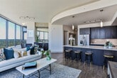 Located at 890 Juniper St NE in Atlanta's vibrant Midtown neighborhood, this high-rise residence delivers an exceptional urban living experience defined by dramatic floor-to-ceiling curved windows and sweeping panoramic views of the Atlanta skyline and surrounding greenery.

The open-concept living area is a standout feature, bathed in abundant natural light and anchored by expansive wraparound windows that frame the city below. Rich hardwood flooring flows throughout, adding warmth to the contemporary aesthetic.

The modern kitchen is thoughtfully designed with dark espresso cabinetry, quartz countertops, a large center island with bar seating, a tile backsplash, and a full suite of stainless steel appliances. Pendant and track lighting complete the polished look.

The bedrooms offer serene retreats with large windows overlooking the cityscape. The primary bedroom includes access to a generously sized walk-in closet with extensive built-in shelving and hanging space. Bathrooms are finished with marble-style tile surrounds, soaking tubs, and dark cabinetry accents.

Additional highlights include an in-unit laundry area with a side-by-side washer and dryer, dedicated storage shelving, and a consistent palette of neutral tones that enhance the bright, airy atmosphere throughout the residence.