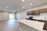 Located on NW Marconi Lane in Waukee, Iowa, this well-designed single-story home offers a thoughtful layout with four bedrooms, two bathrooms, and a dedicated laundry room. The open-concept kitchen and living area serves as the heart of the home, featuring a large center island with a white quartz countertop, dark-toned shaker-style cabinetry, a full suite of stainless steel appliances including a range, microwave, dishwasher, and refrigerator, and recessed lighting throughout. Wood-look luxury vinyl plank flooring extends across the main living areas, adding warmth and continuity. The spacious living room flows naturally from the kitchen and is filled with natural light from a sliding glass door that opens to the outdoors. The bedrooms offer a mix of vinyl plank and plush carpet flooring, with large windows that frame pleasant neighborhood views and allow abundant natural light. The primary bedroom provides a comfortable and private retreat. Both bathrooms are finished with dark wood vanities, white countertops, and wood-look flooring. A hallway connects the bedrooms and living spaces with clean, neutral walls and recessed lighting. The dedicated laundry room houses a full-size washer and dryer with overhead shelving for added storage convenience.