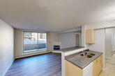 Located at 10411 105 Avenue NW in Edmonton, Alberta, this one-bedroom, one-bathroom unit offers a well-considered layout across a single floor. The open-concept living and kitchen area serves as the heart of the space, where light-toned cabinetry with grey laminate countertops and a double-basin sink define the kitchen zone. A structural column elegantly separates the kitchen from the living area, which features hardwood-style flooring, a corner fireplace with a clean white mantel, and a large sliding glass door that opens to an outdoor patio and brings in ample natural light with views of the surrounding neighbourhood. The bedroom is a comfortable size, featuring a sliding mirrored closet door, a window with vertical blinds, and the same hardwood-style flooring. An additional closet provides extra storage. The bathroom includes a wide vanity with a mirror cabinet, light wood cabinetry, grey countertop, tile flooring, and a tub-shower combination. A dedicated laundry room houses a stacked washer and dryer unit. Textured ceilings are consistent throughout, and the neutral colour palette gives the space a clean, functional aesthetic throughout.