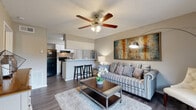 This single-floor residence offers a cohesive and functional layout designed for comfortable everyday living. The open-concept living area serves as the heart of the home, featuring durable wood-look flooring, neutral-toned walls, and a ceiling fan with integrated lighting. A plush area rug anchors the seating space, which flows naturally toward the kitchen. The kitchen is separated by a half-wall breakfast bar with room for bar stools, making it ideal for casual dining or entertaining. It is equipped with black appliances, including a refrigerator and electric range, complemented by white cabinetry and a tasteful subway tile backsplash that adds a modern touch. A dedicated closet area provides built-in shelving for additional storage. The bedroom is a restful retreat, carpeted for warmth and comfort, with a ceiling fan overhead and a window that allows natural light to filter in, creating a bright and welcoming atmosphere. The bathroom is finished in a clean, classic style, featuring a tiled tub-and-shower combination, wood-look flooring, and crisp white walls. Throughout the space, consistent design choices in lighting and neutral tones contribute to a cohesive and inviting ambiance.