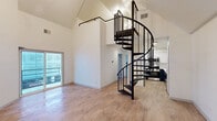 Located in the heart of downtown Austin at 201 E 4th St, this two-story, 2-bedroom, 3-bathroom home offers a thoughtfully designed layout spread across two floors. The main level immediately impresses with soaring vaulted ceilings and an open-concept living area bathed in natural light from a sliding glass door that opens to a balcony. Light wood-tone flooring runs throughout, complementing the bright white walls and creating a clean, modern aesthetic. A striking black spiral staircase serves as the architectural centerpiece, connecting the main level to the upper floor and loft area. The kitchen features navy blue cabinetry with modern black hardware and stainless steel appliances. Upstairs, the loft sits beneath a dramatic angled roofline and is illuminated by a contemporary pendant light fixture. The bedrooms are well-proportioned, with the primary bedroom offering a walk-in closet. The bathrooms are finished with white subway tile, and at least one features a stylish navy vanity with a white countertop, black fixtures, and a well-lit mirror — echoing the home's consistent modern design language. With two hallways providing practical flow between spaces, this home combines urban convenience with dynamic, multi-level living.