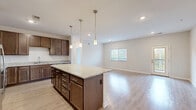 This well-appointed 2-bedroom, 2-bathroom single-floor residence in Mukwonago, WI offers a thoughtfully designed open-concept layout. The combined kitchen and living area serves as the heart of the home, anchored by a large granite-topped center island with rich dark cabinetry and gold-toned hardware. Pendant lighting above the island adds warmth, while stainless steel appliances, ample cabinetry including a full-height pantry, and generous counter space make the kitchen highly functional. The living area flows naturally from the kitchen, featuring light hardwood-style flooring and large windows that bring in natural light and offer views of the surrounding greenery. A private balcony extends the living space outdoors. Both bedrooms are carpeted and well-sized, each featuring large windows with wooded views and dedicated closet space. The primary bedroom includes its own closet with built-in shelving and hanging rods. Four closets throughout provide excellent storage. A dedicated laundry area and a connecting hallway complete the layout. The overall design balances neutral tones, modern finishes, and practical functionality, creating a bright and comfortable living environment.