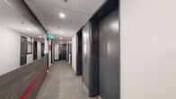 This hallway is located on the fourth floor of the building at 1420 Rue Crescent in Montréal, Quebec. The corridor follows a linear layout, providing access to multiple numbered units as well as elevator lobbies on both ends. The design is contemporary and functional, characterized by a cohesive dark grey and white color palette punctuated by bold red accents.

The walls feature a combination of smooth painted surfaces and large-format dark wood-effect tiles, with a distinctive horizontal red tile stripe running along the lower portion of the tiled sections, adding a striking visual detail. Dark grey elevator doors and unit entry doors with brushed hardware complement the overall aesthetic. A large mirror near the elevator lobby enhances the sense of space within the corridor.

Underfoot, grey loop-pile carpet tiles with subtle red linear detailing provide a durable and practical flooring solution throughout. Recessed ceiling lighting delivers consistent, even illumination along the length of the hallway. Safety infrastructure is prominently integrated, including clearly marked emergency exit signs, fire extinguisher cabinets, fire hose stations, and a pull station, all positioned for easy visibility and access. The overall ambiance is clean, modern, and efficiently designed.