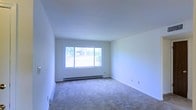 This single-floor space presents a clean, minimalist interior centered around a generously sized open room. The walls are finished in crisp white, contributing to a bright and airy atmosphere throughout. Neutral-toned wall-to-wall carpeting covers the floor, providing a soft and practical surface underfoot.

A large sliding window serves as the focal point of the main room, allowing abundant natural light to flood the interior while framing views of lush outdoor greenery and trees beyond. The window design maximizes the connection between the interior and the natural surroundings outside.

A baseboard heating unit runs along the wall beneath the window, offering an efficient and unobtrusive climate control solution. The room's smooth, flat white ceiling maintains a clean visual line throughout the space.

The overall layout is open and versatile, offering flexibility for a variety of uses and furniture arrangements. The combination of white walls, neutral carpeting, and ample natural light creates a calm, neutral palette well-suited to a range of interior styles. The space presents a blank canvas ready for personalization.