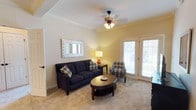 This single-floor unit at Overbrook Apartments offers a thoughtfully designed layout that balances functionality and comfort throughout. The living room serves as the heart of the space, featuring warm neutral walls, crown molding, plush carpeting, and a ceiling fan with light fixture. Double doors allow natural light to fill the room and provide access to an outdoor area. The adjoining dining area is defined by a tray ceiling with crown molding and is anchored by an elegant chandelier above a glass-topped table, with the kitchen visible nearby.

The kitchen is equipped with rich wood cabinetry, light countertops, a tile backsplash, and black appliances including a refrigerator, electric range, and over-the-range microwave, providing ample storage and counter space.

Both bedrooms are carpeted and receive natural light through large windows with blinds. The primary bedroom offers generous space, while the secondary bedroom includes room for a desk area. Each bathroom mirrors the other in design, featuring warm wood cabinetry with stone-tone countertops, a single vanity, and a tub-shower combination with tile flooring throughout.