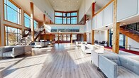 Located at 90 Journey Rd in Seneca, South Carolina, this impressive two-story building offers a substantial total floor area spread evenly across both levels, making it a well-proportioned and highly functional communal space. The architectural design blends modern construction with warm, rustic elements — most notably the exposed natural wood columns and beams that frame the interior throughout both floors.

The ground floor makes an immediate impact with its dramatic double-height ceilings and expansive floor-to-ceiling windows framed in warm wood, flooding the space with abundant natural light and offering sweeping outdoor views. Light hardwood flooring anchors the open main living area, which is furnished with contemporary seating arrangements ideal for gathering and socializing. A striking wood-and-steel staircase connects the two floors, serving as both a functional and architectural centerpiece.

The upper level features rich red-toned carpeting that continues through its corridors and living areas. An open mezzanine overlooks the ground floor below, lined with a natural wood railing. This floor includes an additional lounge area with plush seating, a TV, and continued access to large windows framing outdoor views. Seating nooks, casual dining areas with communal tables, and smaller breakout spaces are distributed throughout, providing versatile areas for both relaxation and collaboration. The overall ambiance is bright, welcoming, and thoughtfully designed.