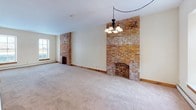 This two-floor space blends classic character with functional design across a well-proportioned layout. The main living area is a standout, featuring two striking exposed brick fireplaces that serve as dramatic focal points, complemented by soft carpeting underfoot and a chandelier overhead. Multiple windows along the wall allow natural light to fill the room, enhancing its warm, inviting atmosphere. A second carpeted living space on the upper level continues the vaulted ceiling design, with an angled roofline adding architectural interest and a window providing additional natural light. Baseboard heating runs throughout the carpeted rooms, ensuring comfort year-round.

The kitchen is efficiently laid out in a galley style, featuring light wood cabinetry, a gas range, a refrigerator, and tile flooring. An electrical panel is conveniently located nearby. The space includes multiple bathrooms, each finished with tile flooring, wood-trimmed mirrors, and vanities with integrated sinks. One bathroom features a tub-shower combination, while others offer similar fixtures in a clean, straightforward style. One bedroom includes a private en-suite bathroom for added convenience. Wood trim detailing throughout the space ties the rooms together cohesively.
