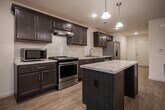 Located at 2749 River Rock Dr in Morristown, Tennessee, this single-floor residence offers a thoughtfully designed layout with consistent light wood-style flooring throughout. The kitchen serves as a central highlight, featuring rich dark espresso cabinetry with brushed nickel hardware, light granite-style countertops, and a full suite of stainless steel appliances including a refrigerator, electric range, microwave, and dishwasher. A center island provides additional prep space, while recessed lighting and pendant fixtures illuminate the area. An open sightline from the kitchen leads toward a windowed dining or living area, allowing natural light to filter through the space. The bedrooms are generously sized, each equipped with ceiling fans with light kits and windows that bring in additional natural light. At least one bedroom includes a walk-in closet with built-in shelving, offering practical storage. The bathroom features dark cabinetry consistent with the kitchen aesthetic, a single-basin vanity with white countertop, a large mirror, and a grab bar for added accessibility. A utility closet houses the HVAC system, and a laundry connection is also present. The overall design presents a clean, functional, and cohesive living environment.
