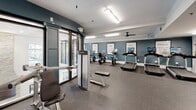 Located at 7000 Johnson Farm Ln in Chadds Ford, PA, this fitness center is a thoughtfully designed, single-floor facility that offers a comprehensive workout experience. The space is defined by its clean, modern aesthetic, featuring teal accent walls, crisp white crown molding, and durable rubber flooring throughout. Motivational framed typography — with phrases like "Spin," "Run," "Rest," and "Crunch" — adorns the walls, reinforcing the energetic atmosphere.

The cardio zone is generously equipped with multiple treadmills and stationary bikes, each outfitted with individual screens for an engaging workout experience. A dedicated cycling and elliptical area provides additional low-impact training options, complemented by natural light from large windows overlooking lush greenery. Ceiling fans contribute to a comfortable environment during intense sessions.

The strength training area features a full rack of dumbbells, weight benches, and a multi-station cable machine, all set against a floor-to-ceiling mirror wall that amplifies the sense of space and allows for proper form checks. Recessed and overhead fluorescent lighting ensures the entire facility is well-illuminated. A seating bench and utility station near the exit add functional convenience, making this fitness center a complete and inviting space for all levels of exercise.