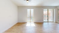 This thoughtfully designed two-bedroom, two-bathroom residence offers a clean, modern aesthetic throughout its single-floor layout. The entrance opens into a hallway with warm wood-look flooring and crisp white walls, setting the tone for the rest of the home.

The combined kitchen and living area serves as the heart of the space. The kitchen is well-appointed with warm wood cabinetry, mosaic tile backsplash, stainless steel appliances including a refrigerator with ice maker, range, and over-the-range microwave, complemented by track lighting overhead. The adjoining living area benefits from a tall window and access to a balcony, flooding the room with natural light and offering views of the surrounding urban landscape.

The primary bedroom is a generously sized retreat featuring a ceiling fan, large sliding glass doors framing bright city views, and rich hardwood-tone flooring. The second bedroom is equally bright and well-proportioned, with its own ceiling fan and closet access.

Both bathrooms echo the home's modern sensibility. One features a wood-framed vanity mirror, wood-toned cabinetry, and a clean white countertop. The second bathroom includes a full soaking tub with a tiled shower surround and built-in niche. A dedicated closet and multiple hallways complete this functional and stylish home.
