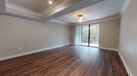 This single-floor residence offers a thoughtfully designed layout that balances open living spaces with functional interior details. The expansive living area immediately draws the eye with its rich, dark hardwood-style flooring, neutral-toned walls, and elegant crown molding that frames the tray ceiling. Structural beams add architectural character overhead, while a central ceiling fixture provides warm ambient lighting. Floor-to-ceiling sliding glass doors lead to a private balcony overlooking lush tree canopy, flooding the room with natural light and bringing the outdoors in.

The galley-style kitchen is outfitted with dark espresso cabinetry, granite-look countertops, and a full suite of stainless steel appliances including a refrigerator, electric range, microwave, and dishwasher. A pass-through opening connects the kitchen to the living area, enhancing the sense of openness and flow throughout.

The bathroom is finished with wood-look flooring, a full soaking tub and shower combination featuring white tile surround accented by a distinctive green tile border, dark wood vanity cabinetry, granite countertops, and brushed nickel hardware. The overall aesthetic of the space is clean and contemporary, with consistent finishes tying each area together cohesively.