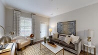 Located at 3825 Ladson Rd in North Charleston, SC, this thoughtfully designed one-bedroom, one-bathroom residence offers a comfortable and stylish single-floor layout. The open-concept living, dining, and kitchen area creates a seamless flow throughout the main living space. The living room features rich hardwood-style flooring, crown molding, and large windows that invite abundant natural light, complemented by a glass-paneled door providing outdoor access. The dining area is defined by an elegant chandelier overhead and warm neutral tones, creating an inviting atmosphere for gatherings. The kitchen is equipped with dark cabinetry, stainless steel appliances, subway tile backsplash, and a granite breakfast bar with pendant lighting — ideal for both cooking and casual dining. The generously sized primary bedroom offers plush carpeting, vaulted ceilings, and direct access to the kitchen area, enhancing the unit's functional flow. A walk-in closet with wire shelving provides ample storage. The bathroom features tile flooring, a shower with curtain enclosure, and granite vanity surfaces. Throughout the residence, crown molding, neutral wall tones, and cohesive finishes contribute to an overall polished and modern ambiance.