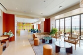 Located at 639 Glen Iris Dr NE in Atlanta's dynamic Old Fourth Ward neighborhood, this thoughtfully designed amenity space delivers a bold and energetic atmosphere across a single, open floor. The interior is anchored by a striking color palette of deep terracotta red, warm cream, and vivid yellow, expressed through accent walls, bold geometric wall graphics, and vibrant accent doors that create visual energy throughout.

The lounge area features curved upholstered seating, leather ottomans, rattan accent chairs, and a mix of round coffee tables with stone and glass tops, all arranged atop textured area rugs to define intimate conversation zones. Overhead, large drum pendant lights provide warm, even illumination complemented by recessed ceiling fixtures.

A dedicated dining and kitchen zone anchors one end of the space, highlighted by a bold yellow-and-red grid-patterned feature wall, a white island with bar seating, green tile backsplash, and multiple dining tables surrounded by sleek dark chairs. Pendant lighting in varied styles adds character to this area.

Floor-to-ceiling glazed walls and sliding glass doors flood the space with natural light and open directly onto an outdoor terrace, offering panoramic views of the Atlanta skyline. Lush indoor greenery is layered throughout, softening the modern design and reinforcing a fresh, welcoming ambiance.