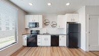 Located at 321 Debaliviere Ave in St. Louis, Missouri, this single-floor unit offers a thoughtfully designed layout with modern finishes and a cohesive, neutral color palette. Light-toned hardwood-style flooring runs throughout the space, lending warmth and visual continuity from room to room.

The kitchen is a standout feature, outfitted with crisp white cabinetry, dark countertops, and a full suite of black appliances including a range, over-the-range microwave, dishwasher, and refrigerator. A classic white subway tile backsplash adds texture, while a large window adjacent to the range floods the area with natural light. Circular decorative shelving accents the walls, adding a modern touch.

A bright, open hallway connects the main living areas, with recessed lighting and multiple white panel doors providing clean transitions between spaces. The living area is generously sized, featuring white walls, light flooring, and neutral tones that create a versatile, move-in-ready canvas.

The bathroom is well-appointed with a white vanity featuring black hardware, a glass-enclosed shower, and consistent wood-look flooring. The overall ambiance of the unit is clean, contemporary, and functional, reflecting a modern residential design sensibility.