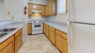 Located at 8600 Cobblefield Drive in Columbia, Maryland, this single-floor residence offers a well-organized and functional layout designed for comfortable everyday living. The kitchen is equipped with warm honey-toned wood cabinetry, ample counter space with light gray laminate surfaces, tile flooring, and a full suite of appliances including an electric range, overhead ventilation hood, and refrigerator. A window above the counter allows natural light to brighten the workspace.

The living area is generously proportioned, featuring neutral wall-to-wall carpeting, vaulted ceilings, and a large window fitted with vertical blinds that invite natural light. Track lighting accents the space, adding a practical yet stylish touch. A half-wall partition subtly defines zones within the open layout.

The bedroom is carpeted and includes access to a well-organized walk-in closet outfitted with built-in wooden shelving and hanging rods, offering abundant storage. The bathrooms are clean and bright, with one featuring a wide vanity with white cabinetry, solid surface countertop, and large mirror, while another includes a full tub-shower combination with chrome fixtures and tile surround. Tile flooring runs throughout the wet areas, contributing to a cohesive, easy-to-maintain finish throughout the home.