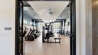 Located at 601 Gilcrest Farm Rd in Wake Forest, NC, this well-appointed fitness center offers a comprehensive workout facility across a single thoughtfully designed floor. The space is divided into two distinct areas: a main exercise room and a dedicated studio or flex space, together providing ample room for a full range of fitness activities.

The main exercise room is finished with a contemporary aesthetic, featuring bold dark and light two-tone walls, recessed lighting, and large floor-to-ceiling steel-framed glass doors and windows that flood the space with natural light and offer views of the outdoors. A ceiling fan adds to the comfort of the workout environment. The room is equipped with a wide selection of cardio machines, including treadmills, ellipticals, and stationary bikes, as well as a robust selection of strength training equipment — cable machines, a squat rack with bench, dumbbells, and weight plates. Mirrored walls in the strength area enhance the sense of space and support proper form.

The adjoining studio room features elegant panel molding, soft neutral tones, and a wall-mounted barre alongside full-length mirrors, making it ideal for yoga, cycling, or group fitness classes. Tall windows provide natural light and outdoor views. Together, these two spaces form a polished, fully functional fitness facility suited for a wide variety of training needs.