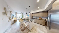 Located at 1050 Blanche St in West Palm Beach, FL, this well-appointed 2-bedroom, 2-bathroom residence offers a thoughtfully designed single-floor layout with modern finishes throughout. The open-concept kitchen, dining, and living area serves as the heart of the home, anchored by a center island with a dark quartz countertop and seating for two beneath sleek black pendant lights. The kitchen features light wood cabinetry extending to the ceiling, a classic subway tile backsplash, and stainless steel appliances. Light-toned tile flooring flows seamlessly through the main living areas, enhancing the bright, airy atmosphere. The living room opens to a private balcony offering elevated views of a resort-style pool deck lined with palm trees. The primary bedroom is a comfortable retreat with plush carpeting, a natural light-filled window, and generous closet space. The second bedroom features a ceiling fan, a tray ceiling detail, and a vibrant accent wall. Both bathrooms are finished with wood-toned vanities and stone countertops — the primary bath includes a glass-enclosed walk-in shower with a backlit mirror, while the second bath offers a clean, functional design. Additional conveniences include an in-unit laundry area and a dedicated entrance.