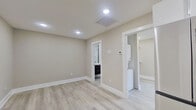 This thoughtfully designed single-floor unit offers a clean, contemporary aesthetic throughout, characterized by light gray vinyl plank flooring, neutral warm-toned walls, and crisp white baseboards that lend a polished, cohesive feel to every room.

The kitchen is a standout feature, equipped with a full suite of stainless steel appliances including a refrigerator, range, microwave, and dishwasher. White upper cabinetry pairs with dark lower cabinets, complemented by a striking geometric-patterned tile backsplash that adds visual depth and modern character to the space.

The main living area is open and airy, illuminated by recessed lighting and benefiting from a practical, flexible layout. Adjacent to the main room is a generously sized walk-in closet outfitted with dual hanging rods and shelving, providing ample storage. A stacked in-unit washer and dryer is conveniently positioned nearby, adding everyday practicality.

The bathroom is elegantly finished, featuring a large glass-enclosed walk-in shower adorned with classic white subway tile walls, penny-round mosaic tile flooring, and a built-in niche. A frosted window allows natural light to filter in while maintaining privacy. A dark-cabinetry vanity completes the bathroom's refined, contemporary look.