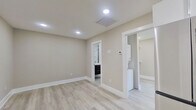 This thoughtfully designed single-floor unit offers a clean, contemporary aesthetic throughout, characterized by light gray vinyl plank flooring, neutral warm-toned walls, and crisp white baseboards that lend a polished, cohesive feel to every room.

The kitchen is a standout feature, equipped with a full suite of stainless steel appliances including a refrigerator, range, microwave, and dishwasher. White upper cabinetry pairs with dark lower cabinets, complemented by a striking geometric-patterned tile backsplash that adds visual depth and modern character to the space.

The main living area is open and airy, illuminated by recessed lighting and benefiting from a practical, flexible layout. Adjacent to the main room is a generously sized walk-in closet outfitted with dual hanging rods and shelving, providing ample storage. A stacked in-unit washer and dryer is conveniently positioned nearby, adding everyday practicality.

The bathroom is elegantly finished, featuring a large glass-enclosed walk-in shower adorned with classic white subway tile walls, penny-round mosaic tile flooring, and a built-in niche. A frosted window allows natural light to filter in while maintaining privacy. A dark-cabinetry vanity completes the bathroom's refined, contemporary look.