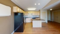 Located at 1720 13th St SE in Minot, North Dakota, this single-floor residence offers a well-organized layout designed for comfortable everyday living. The open-concept kitchen is a central highlight, featuring light maple cabinetry, dark granite-style countertops, and a full suite of black appliances including a refrigerator, range, microwave, and dishwasher. A kitchen island provides additional workspace and storage, while hardwood-style flooring extends throughout the main living areas. Vaulted ceilings in the kitchen and living space enhance the sense of openness, and a sliding glass door leads directly to an outdoor balcony, filling the area with natural light and offering pleasant views of the surrounding landscape. The bedrooms are carpeted for warmth and comfort, each featuring windows that frame open outdoor views and baseboard heating units. The bathrooms are finished with wood-toned vanity cabinetry, dark countertops, and chrome fixtures, maintaining a consistent design palette throughout. Warm neutral tones on the walls create a cohesive and inviting atmosphere across all rooms. The thoughtful floor plan, as visible in the 3D model, connects living, dining, and private spaces in a practical and accessible single-level arrangement.