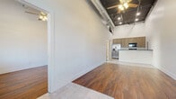 This single-story space in Leeds, Alabama, showcases a compelling blend of industrial and contemporary design elements throughout. The standout architectural feature is the dramatic ceiling height, which creates an expansive, airy atmosphere across the main living areas. Exposed ductwork and a dark corrugated ceiling with ceiling fans and track lighting add a distinctive industrial character, contrasting beautifully with the clean white walls.

Rich, warm-toned hardwood flooring runs throughout the primary living spaces, while light-colored tile floors are found in the kitchen and entry areas. The front entry welcomes natural light through a paneled door with sidelights and transom-style windows positioned high on the walls, reinforcing the sense of vertical space. Exposed original brick columns appear in multiple areas, lending a raw, historic charm to the otherwise modern interior.

The kitchen is well-appointed with light wood cabinetry, dark countertops, stainless steel appliances including a French door refrigerator, a black electric range, and an over-the-range microwave. Additional rooms feature hardwood floors, natural light from windows, and ceiling fans, maintaining a consistent, open aesthetic throughout the space.