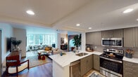 This well-appointed single-floor residence offers a thoughtfully designed open-concept layout that seamlessly connects the kitchen, dining, and living areas. The kitchen is a standout, featuring sleek gray shaker cabinetry, a full suite of stainless steel appliances including a gas range, microwave, and refrigerator, complemented by a striking marble-look quartz waterfall island and a tasteful tile backsplash. Light wood flooring runs throughout, adding warmth and continuity to the space.

The living area is generously proportioned, bathed in natural light, and opens to a dedicated workspace nook accented by a warm amber feature wall, creating a distinct and functional zone. The space is further enriched by an ornate arched floor mirror, lending an eclectic, global-inspired character.

Two bedrooms offer restful retreats with large windows framing impressive urban skyline views. The primary bedroom features a bold teal accent wall adorned with woven basket décor, while the second bedroom benefits from dual corner windows that flood the room with natural light and sweeping cityscape vistas.

Recessed lighting throughout, clean white walls, and a cohesive mix of modern and bohemian design elements give this residence a warm, inviting ambiance ideal for urban living.