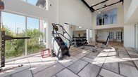 This state-of-the-art fitness center is designed to accommodate a wide range of workout styles within a bright, contemporary setting. The facility is characterized by soaring double-height ceilings and floor-to-ceiling windows that flood the space with natural light while offering views of the surrounding greenery. Large ceiling fans are suspended overhead, enhancing airflow throughout the expansive workout areas.

The flooring transitions between light hardwood and large-format tile, subtly delineating distinct functional zones. A standout feature is the full-height rock climbing wall, accented with colorful handholds and set against a bold patterned backdrop, providing a unique vertical training option. Adjacent to it, a dedicated strength zone houses a Matrix functional training system, weight benches, and a comprehensive dumbbell rack displayed along mirrored walls.

The cardio zone is well-equipped with multiple treadmills, elliptical trainers, stair climbers, and Concept2 rowing machines arranged to maximize space and usability. A separate open-floor studio area with hardwood flooring offers ample room for stretching, yoga, or group fitness activities. The overall ambiance is clean, airy, and energizing, with a modern white palette and generous glazing creating an inviting environment for a comprehensive fitness experience.