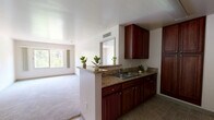 Located on Colorado Boulevard in the Eagle Rock neighborhood of Los Angeles, this one-bedroom, one-bathroom unit offers a practical and well-organized single-floor layout. The open-concept design connects the kitchen directly to the living and dining areas, creating a cohesive and efficient use of space. The kitchen is outfitted with rich dark wood cabinetry, granite-style countertops, a double-basin sink, and a built-in microwave, complemented by a peninsula that serves as a natural divider from the living area. The living room is bright and airy, featuring plush carpeting and a large sliding window that frames views of surrounding greenery, filling the space with natural light. A dedicated dining area sits adjacent to the kitchen for convenient daily living. The bedroom is a comfortable retreat with soft carpeting, a ceiling vent for climate control, and direct access to a dedicated closet. The bathroom features matching dark wood cabinetry, a single vanity with a mirror, tile flooring, and a full shower-tub combination. A bold red entry door adds a distinctive touch to the entryway, which transitions from tile flooring into the carpeted main living areas. Clean white walls throughout create a neutral, move-in-ready ambiance.