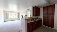 Located on Colorado Boulevard in the Eagle Rock neighborhood of Los Angeles, this one-bedroom, one-bathroom unit offers a practical and well-organized single-floor layout. The open-concept design connects the kitchen directly to the living and dining areas, creating a cohesive and efficient use of space. The kitchen is outfitted with rich dark wood cabinetry, granite-style countertops, a double-basin sink, and a built-in microwave, complemented by a peninsula that serves as a natural divider from the living area. The living room is bright and airy, featuring plush carpeting and a large sliding window that frames views of surrounding greenery, filling the space with natural light. A dedicated dining area sits adjacent to the kitchen for convenient daily living. The bedroom is a comfortable retreat with soft carpeting, a ceiling vent for climate control, and direct access to a dedicated closet. The bathroom features matching dark wood cabinetry, a single vanity with a mirror, tile flooring, and a full shower-tub combination. A bold red entry door adds a distinctive touch to the entryway, which transitions from tile flooring into the carpeted main living areas. Clean white walls throughout create a neutral, move-in-ready ambiance.