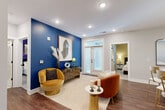Located at 2408 South Blvd in Charlotte's Dilworth neighborhood, this well-appointed 2-bedroom, 3-bathroom residence offers a thoughtfully designed single-level layout. Rich hardwood flooring flows through the entrance and into the open-concept kitchen and living area, where recessed lighting and a striking gold chandelier set an inviting ambiance. The kitchen features slate-blue cabinetry with gold hardware, white quartz countertops, a geometric tile backsplash, and stainless steel appliances. The living room makes a bold statement with a deep blue accent wall, French doors opening to a private balcony, and generous natural light. Each bedroom offers plush carpeting, ceiling fans, large windows with blinds, and vibrant accent walls — one in warm beige, one in bold violet. Both bedrooms include walk-in closets with wire shelving systems. The bathrooms are elegantly finished with marble-style tile floors, slate-blue floating vanities, gold and matte black fixtures, and large mirrors. Additional spaces include a dedicated office, laundry room, utility room, and two closets, ensuring ample storage and functional versatility throughout.