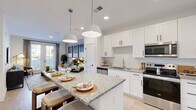 Located at 1 Hatcher Drive in Stockbridge, GA, this one-bedroom, one-bathroom residence offers a thoughtfully designed single-floor layout that maximizes every square foot. The open-concept kitchen is a standout feature, showcasing crisp white shaker cabinetry with matte black hardware, granite countertops, a herringbone-patterned tile backsplash, and a full suite of stainless steel appliances including a range, microwave, dishwasher, and refrigerator. A central island with pendant lighting provides additional prep space and casual seating. Light wood-style flooring flows seamlessly throughout, connecting the kitchen to the bright living room, which features recessed lighting, a wall-mounted TV setup, and French doors that invite natural light and outdoor views. The bedroom offers a comfortable retreat with a ceiling fan, large window with outdoor views, and a dedicated closet with built-in storage. The bathroom mirrors the home's modern aesthetic with granite countertops, white cabinetry, and in-unit stacked laundry conveniently integrated into the space. Clean white walls and consistent finishes throughout create a cohesive, contemporary ambiance.