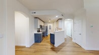 This three-story home offers a thoughtfully designed layout spread across three distinct levels. The ground floor provides an attached garage with automatic opener, offering secure parking and additional storage. The main living level serves as the heart of the home, showcasing an open-concept kitchen and living room highlighted by warm hardwood-style flooring throughout. The kitchen features two-tone cabinetry — navy blue lower cabinets paired with light upper cabinets — complemented by white quartz countertops, stainless steel appliances including a refrigerator, range, microwave, and dishwasher, plus a peninsula for additional workspace. A pantry and dedicated laundry area add everyday convenience. The living room is anchored by a classic white-framed fireplace and large windows that invite natural light and views of surrounding greenery. A balcony extends the living space outdoors, overlooking lush landscaping. The upper floor houses both bedrooms, including a spacious primary suite with its own closet. The two bathrooms are finished with gray shaker-style cabinetry, white countertops, large mirrors, and hardwood-style flooring, with one featuring a sliding-glass enclosed shower. Carpeted staircases connect each level, and multiple closets provide ample storage throughout.