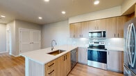 This thoughtfully designed two-bedroom, one-bathroom residence offers a comfortable and modern living experience across a single floor. The open-concept kitchen and living area serves as the heart of the home, showcasing light wood cabinetry with sleek black hardware, a white quartz peninsula with an undermount sink, and a full suite of stainless steel appliances including a refrigerator, electric range, over-the-range microwave, and dishwasher. A classic white subway tile backsplash adds a clean, polished touch, while light wood-tone flooring flows throughout the main living spaces, enhancing the bright and airy atmosphere. Recessed lighting illuminates the kitchen and living area effectively. The living room features a glass door opening to a private balcony with scenic outdoor views of trees and surrounding landscape. Both bedrooms are carpeted, bathed in natural light through large windows, and offer restful retreats with neutral wall tones. The primary bedroom is generously sized and includes access to a closet. The bathroom is clean and functional, appointed with a full soaking tub and shower combination, wood-look flooring, and a vanity with a light countertop. The overall aesthetic is clean, contemporary, and move-in ready.