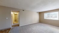This single-floor, 2-bedroom, 1-bathroom unit offers a functional and straightforward layout across a compact but well-organized footprint. Neutral beige walls and textured ceilings are consistent throughout, creating a cohesive and understated aesthetic. Plush wall-to-wall carpeting covers the living areas and bedrooms, adding warmth underfoot, while the kitchen and bathroom feature tile flooring.

The spacious primary bedroom is notably generous in size, featuring a large window that admits natural light and provides outdoor views. A hallway with built-in shelving offers convenient storage access. The second bedroom, also carpeted, includes a window and connects to the central hallway.

The kitchen is equipped with white cabinetry extending to the ceiling, a granite-patterned countertop, a stainless sink, a dishwasher, an electric range, and a full-size refrigerator, all illuminated by a flush ceiling light panel. The tile flooring in a warm stone pattern complements the white cabinetry.

The bathroom features a wide vanity with a granite-style countertop, white cabinetry below, a large wall mirror, subway tile walling, and tile flooring. A hallway connects all rooms, ensuring efficient circulation throughout the unit.