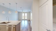 This thoughtfully designed one-bedroom, one-bathroom residence offers an efficient and functional layout across a single floor. The open-concept living and kitchen area is anchored by a standout kitchen featuring taupe shaker-style cabinetry, granite countertops, a herringbone tile backsplash, and a full suite of stainless steel appliances including a refrigerator with ice maker, range, microwave, and dishwasher. A peninsula island with pendant lighting provides additional prep space and casual seating. Durable wood-style flooring runs throughout the main living areas, while a ceiling fan and sliding glass doors allow for natural light and outdoor access. The bedroom offers a carpeted floor, a window with outdoor views, and connects directly to the full bathroom and a spacious walk-in closet outfitted with built-in shelving and multiple hanging rods. The bathroom features a tile-surround glass-enclosed shower and hardwood flooring. A dedicated laundry area houses a front-loading Whirlpool washer with additional shelving overhead. Clean white walls, neutral tones, and a bright, airy ambiance give this residence a polished, move-in-ready feel throughout.