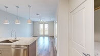 This thoughtfully designed one-bedroom, one-bathroom residence offers an efficient and functional layout across a single floor. The open-concept living and kitchen area is anchored by a standout kitchen featuring taupe shaker-style cabinetry, granite countertops, a herringbone tile backsplash, and a full suite of stainless steel appliances including a refrigerator with ice maker, range, microwave, and dishwasher. A peninsula island with pendant lighting provides additional prep space and casual seating. Durable wood-style flooring runs throughout the main living areas, while a ceiling fan and sliding glass doors allow for natural light and outdoor access. The bedroom offers a carpeted floor, a window with outdoor views, and connects directly to the full bathroom and a spacious walk-in closet outfitted with built-in shelving and multiple hanging rods. The bathroom features a tile-surround glass-enclosed shower and hardwood flooring. A dedicated laundry area houses a front-loading Whirlpool washer with additional shelving overhead. Clean white walls, neutral tones, and a bright, airy ambiance give this residence a polished, move-in-ready feel throughout.