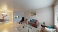 This single-floor residence offers a cohesive and comfortable layout designed for everyday living. The living room serves as the heart of the home, featuring light tile flooring, neutral walls, and a large window that invites natural light. The space is open and welcoming, with room for multiple seating arrangements centered around a glass coffee table. A decorative abstract canvas adds a touch of color and personality to the room.

The kitchen is efficiently designed with dark cabinetry, granite-style countertops, black appliances including a refrigerator and dishwasher, and a stainless steel sink. It connects directly to a cozy dining area, which features tile flooring, a glass-top dining table for four, and an elegant multi-bulb chandelier overhead. A sunburst mirror on the wall adds a stylish focal point to the dining space.

The bedroom is generously proportioned, highlighted by a ceiling fan with integrated lighting, a large window with blinds providing natural light and privacy, and light tile flooring throughout. It comfortably accommodates a queen-size bed and a full dark-wood dresser set.

The bathroom features a granite-style countertop vanity with dark wood cabinetry, a framed mirror, and clean, functional finishes that complete the overall well-maintained character of this residence.