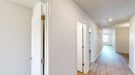Located at 111 NW 63rd Ave in Highfill, Arkansas, this single-story home offers an efficient and practical layout across six bedrooms and two full bathrooms. The interior is unified by warm wood-look flooring that runs throughout the entire home, complemented by crisp white walls and clean white trim for a bright, cohesive aesthetic.

The kitchen is well-appointed with gray shaker-style cabinetry, white countertops, a double-basin sink, and a full suite of black appliances including a refrigerator, electric range with overhead microwave, and dishwasher. The adjacent living area provides a comfortable open feel, featuring a ceiling fan with light kit and large windows that admit generous natural light and outdoor views.

Each of the six bedrooms maintains a consistent design with wood-look flooring, ceiling fans, and windows with blinds that bring in natural light. The spacious primary bedroom offers a notably comfortable footprint among the six. The remaining bedrooms are well-suited for a variety of uses.

Both bathrooms are identically appointed, featuring gray vanity cabinetry, white countertops, a single-basin sink, a tub/shower combination, and wood-look flooring. Additional cabinetry above the toilet provides practical storage. The home's long central hallway connects all rooms efficiently, making this a highly functional property suited for large households or shared living arrangements.