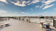Located in Philadelphia's vibrant Fishtown neighborhood, this rooftop deck at 2120 E York St offers an impressive outdoor retreat with sweeping, unobstructed views of the Philadelphia city skyline. The generously sized deck is finished with light gray composite decking that extends across its considerable length, providing a clean, low-maintenance surface built for durability and year-round appeal.

Encircled by sleek black metal railings, the space is thoughtfully designed for both safety and aesthetic cohesion. Multiple distinct seating areas are arranged throughout the deck, furnished with contemporary outdoor chairs, loungers, and round bistro tables that invite relaxation and social gathering. Potted plants and greenery are strategically placed along the perimeter, adding a natural, welcoming touch to the urban setting.

The panoramic views are a defining feature of this rooftop, offering sightlines across the Philadelphia skyline in multiple directions, including the downtown Center City high-rises and the broader tapestry of the city's rooftops and historic church spires. The open sky above ensures an abundance of natural light throughout the day, making the space ideal for enjoying sunrises, sunsets, and clear blue-sky afternoons. A dedicated mechanical area houses the building's HVAC infrastructure, keeping utilities efficiently organized and separate from the deck's recreational zones.