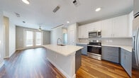 Located at 1614 Hill St in Grand Prairie, TX, this well-designed 2-bedroom, 2-bathroom single-story home offers a thoughtful layout with modern finishes throughout. The open-concept kitchen and living area serves as the heart of the home, anchored by a spacious center island with a white quartz countertop and an undermount sink. The kitchen is equipped with stainless steel appliances, including a French door refrigerator, electric range, and microwave, complemented by two-tone cabinetry — white upper cabinets paired with slate-blue lower cabinets — and a classic subway tile backsplash. Pendant lighting and recessed lights illuminate the space, while warm hardwood-style flooring flows throughout the main living areas. The living room is bright and airy, featuring a ceiling fan and French doors that open to an outdoor balcony, inviting natural light and outdoor views. Both bedrooms are carpeted for comfort and include dedicated closets with built-in shelving and hanging rods. The bathrooms feature clean white vanities with quartz countertops, pendant lighting, and hardwood-style flooring. Neutral tones and clean lines give the entire home a cohesive, contemporary feel.