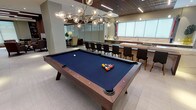 This thoughtfully designed amenity floor offers a diverse range of social and recreational spaces united by a cohesive modern aesthetic. The open-plan main area anchors the floor, featuring a full-sized billiards table beneath a sculptural multi-globe chandelier, complemented by a generous gourmet kitchen. The kitchen showcases an elongated waterfall-edge marble island with an integrated gas cooktop, warm wood cabinetry, stainless steel appliances, a beverage cooler, and a full wall of frosted windows that diffuse natural light across the marble countertops.

A comfortable lounge area features floor-to-ceiling windows dressed with roller shades, a leather sofa, and a striking linear gas fireplace framed by a dramatic floor-to-ceiling slatted wood accent wall. Recessed linear lighting and wood slat ceiling panels throughout the main space add warmth and architectural interest.

A dedicated private screening room provides a true cinema experience, equipped with a large projection screen, overhead projector, and rows of plush upholstered lounge chairs with built-in cup holders, set against warm ambient wall sconces. The floor also includes spaces accessed through sleek black-framed glass partition walls, with rich wood-panel sliding doors adding a refined, functional element throughout.