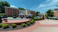 This single-floor commercial office space is situated within a well-maintained multi-story brick building, featuring a welcoming exterior with a covered entry pavilion, manicured landscaping, brick-lined walkways, and ample on-site parking. The building's classic architectural design blends traditional brick facades with modern elements, creating a professional and polished first impression.

Inside, the office layout offers a functional and adaptable environment suited for a variety of professional uses. Corridors are finished with patterned, plaid-style carpeting in neutral tones that carries throughout the interior spaces, complemented by clean white walls and warm wood-toned baseboards and door frames. Frosted glass panel doors add a contemporary touch while maintaining privacy between areas.

Individual offices and open work areas are uniformly finished with the same neutral palette, providing a blank canvas for customization. Each room is equipped with multiple electrical outlets positioned conveniently along the walls, and recessed ceiling lighting ensures consistent, even illumination throughout. Select areas benefit from exterior-facing windows that bring in natural light, enhancing the overall brightness of the workspace.

The space maintains a clean, move-in-ready condition with a straightforward, efficient layout designed to accommodate diverse office configurations and professional environments.