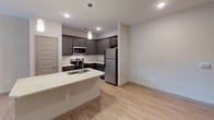 Located at 1820 Gold Hill Rd in Fort Mill, SC, this single-floor unit offers a well-designed, contemporary layout with a cohesive mix of materials and finishes. The open-concept living and kitchen area serves as the heart of the space, where light wood-style flooring flows seamlessly underfoot. A ceiling fan overhead and glass French doors leading to a private balcony fill the living area with natural light and outdoor views of the surrounding greenery.

The kitchen is thoughtfully appointed with dark gray cabinetry, a white subway tile backsplash, light quartz countertops, and a full suite of stainless steel appliances including a refrigerator, electric range, and microwave. A peninsula with an integrated sink and pendant lighting provides additional workspace and casual seating potential, creating a functional connection between the kitchen and living areas.

The bedroom features plush neutral carpeting, a ceiling fan with light fixture, and a window fitted with blinds for natural light and privacy. Paneled doors with a warm taupe finish are consistent throughout the unit, lending a cohesive aesthetic.

The bathroom includes patterned tile flooring, a soaking tub with shower, dark vanity cabinetry with a white countertop, and a large mirror, offering a clean and functional design. Overall, the unit presents a modern, well-maintained living environment.