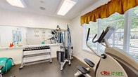 Located at 126 Candlewood Way in Newport News, Virginia, this dedicated exercise room delivers a comprehensive fitness facility within a single, efficiently designed space. The room features durable speckled rubber flooring throughout, providing a safe and practical surface suited for a wide range of workout activities. Overhead fluorescent lighting, complemented by a ceiling-mounted speaker, ensures the space is well-lit and functional at any hour.

The room is outfitted with a diverse selection of equipment, including a treadmill, an elliptical trainer (CTS 375EL by TuffStuff), a multi-station cable weight machine, a dumbbell rack with a full set of free weights, a balance ball, and an ab/back extension bench. A large wall mirror spans one side of the room, visually expanding the space and allowing users to monitor their form during exercise. A wall-mounted flat-screen television adds entertainment convenience during workouts.

Natural light filters in through a window dressed with white blinds and a gold valance curtain, offering a view of the surrounding outdoor greenery. Decorative coastal-themed artwork adorns the walls, contributing to an inviting atmosphere. A French-paned interior door leads to an adjoining restroom, adding practical convenience. A digital scale is also present on the floor. The space is neatly maintained and thoughtfully arranged to maximize usability.