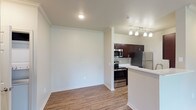 This 1-bedroom, 1-bathroom residence is thoughtfully designed to maximize both function and comfort across a single-floor layout. The open-concept living area features rich wood-style hard flooring, crown molding accents, and a sliding glass door that fills the space with natural light while providing access to an outdoor area with greenery views. The kitchen is well-equipped with dark espresso cabinetry, white countertops, a full suite of stainless steel appliances including a range, microwave, and refrigerator, and a peninsula with pendant track lighting that creates a natural divide from the living area. The bedroom offers a calm retreat with plush carpeting, a ceiling fan with light fixture, and a generously sized window overlooking lush outdoor greenery, allowing for excellent natural light and ventilation. The bathroom is finished with matching dark espresso cabinetry, a white countertop vanity, a large mirror with overhead lighting, and wood-style flooring that carries the design language throughout. A walk-in closet is accessible directly from the bathroom, providing practical storage. The overall aesthetic is clean and contemporary, with neutral tones, consistent finishes, and a cohesive design that creates a comfortable, move-in-ready living environment.