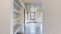 This 1-bedroom, 1-bathroom loft in Memphis, TN showcases an industrial-chic aesthetic rooted in architectural character. Polished concrete floors run throughout the entire space, complementing the exposed structural beams and ductwork on the ceilings, which lend an open, airy quality to every room. Large black-framed windows flood the living areas with natural light and offer views of the surrounding cityscape, enhancing the loft's spacious feel.

The kitchen is a standout feature, equipped with rich dark wood upper cabinetry contrasted by crisp white lower cabinets, a marble-style quartz backsplash and countertops, and a central island that provides both workspace and casual dining. Pendant lighting above the island adds a polished finishing touch.

The bedroom continues the open, light-filled character of the unit, with black-framed windows and ample wall space. Built-in shelving in the hallway area offers practical storage solutions integrated seamlessly into the design.

The bathroom is well-appointed with large-format tile flooring, an extended vanity with generous counter space and under-sink cabinetry, a wide mirror with globe lighting, and a glass-enclosed walk-in shower adorned with soft blue-green subway tile — providing a clean, spa-like atmosphere throughout.