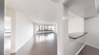 Located at 3130 N Lake Shore Dr in Chicago's Lakeview neighborhood, this one-bedroom, one-bathroom unit offers a well-organized layout across a single floor. The open-plan living area features rich hardwood flooring and a wall of large, floor-to-ceiling windows fitted with horizontal blinds, flooding the space with natural light and offering views of the surrounding cityscape and nearby marina. The kitchen is accessible via a breakfast bar counter and is equipped with dark wood cabinetry, glass-front upper cabinets, black appliances including a refrigerator, electric range, and microwave, along with a stainless steel sink. The spacious bedroom continues the hardwood flooring and shares the same generous window design, with a built-in wall unit air conditioner and a wide closet for ample storage. The bathroom features classic white subway tile surrounding a full bathtub and shower, a dark wood vanity with an integrated sink, patterned mosaic tile flooring, and chrome fixtures. Throughout the unit, clean white walls and consistent flooring create a cohesive, bright, and functional living environment well-suited to urban life along Chicago's lakefront.